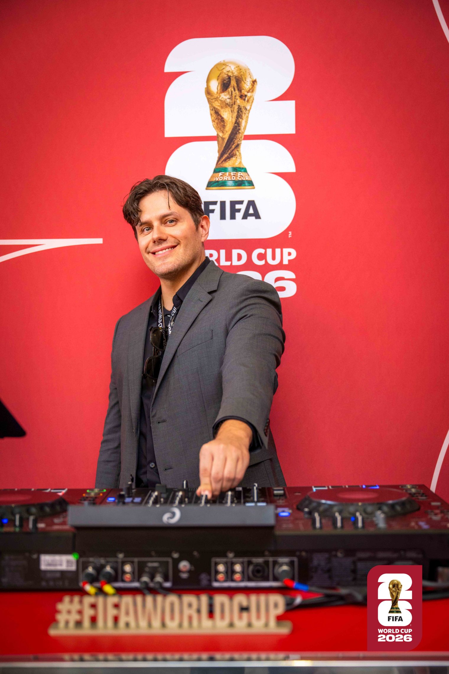 Elvis Suarez DJing at the FIFA World Cup with the trophy and official event branding behind him.